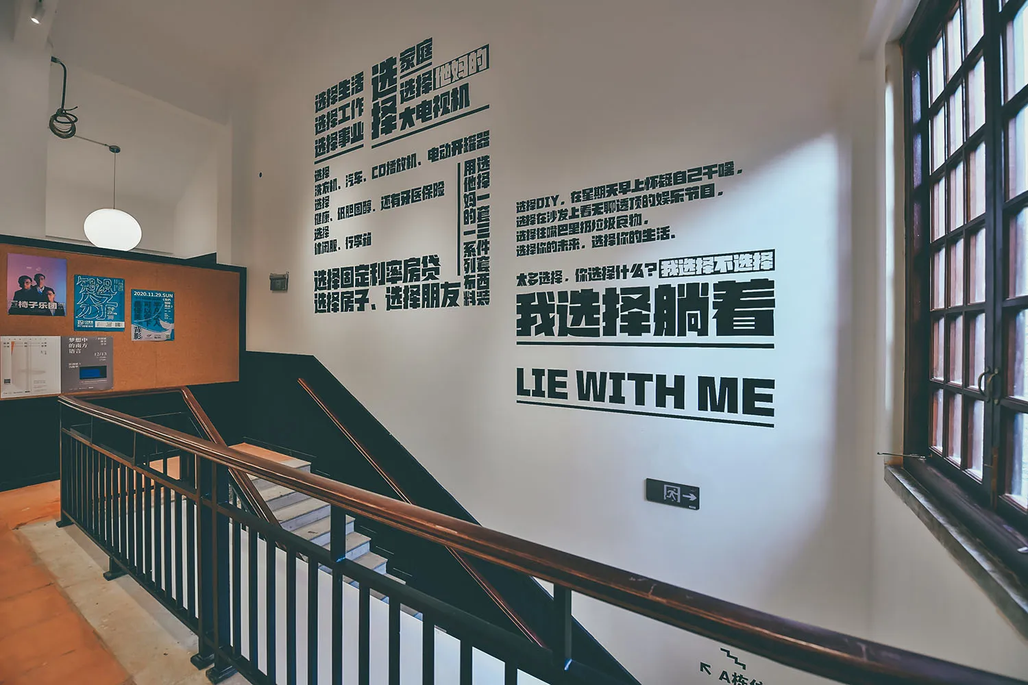 Text-based graphic design printed on a white wall with a staircase in the foreground, featuring various Chinese characters an