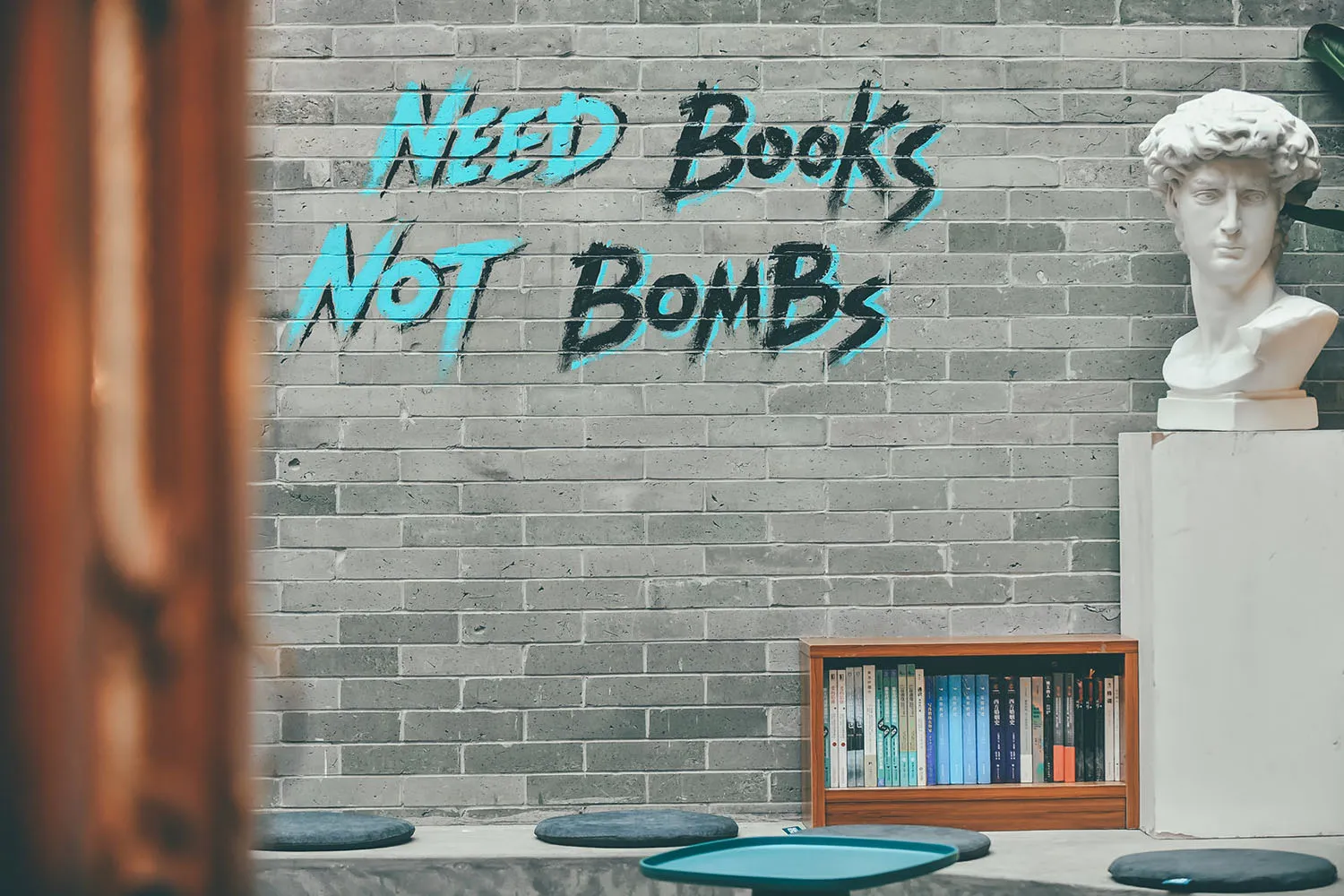 A minimalist library interior with a concrete wall, shelves filled with books, and a bust sculpture.
