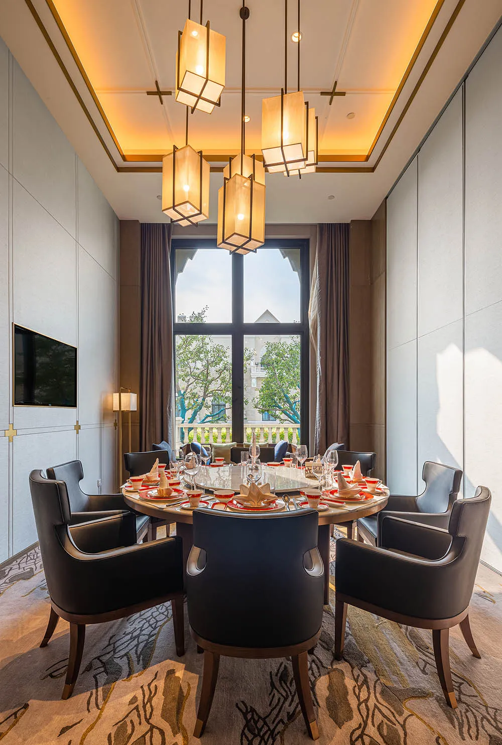 An industrial dining room featuring a large round table surrounded by black chairs, set with red and white tableware on a pat