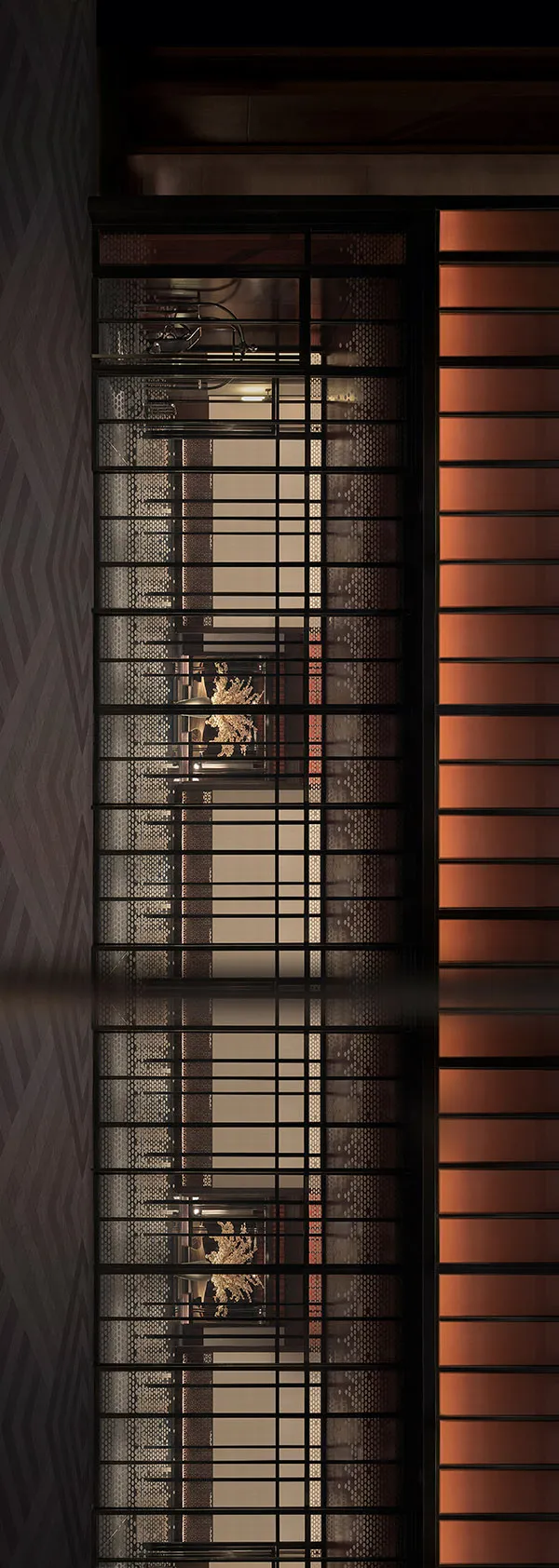 A close-up view of a metal grid window with a warm, inviting interior visible through the mesh.