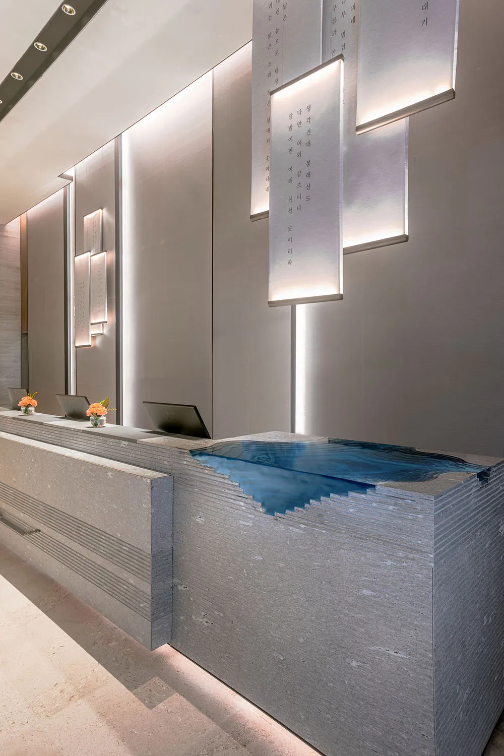 A minimalist reception desk made of concrete with a blue water feature.