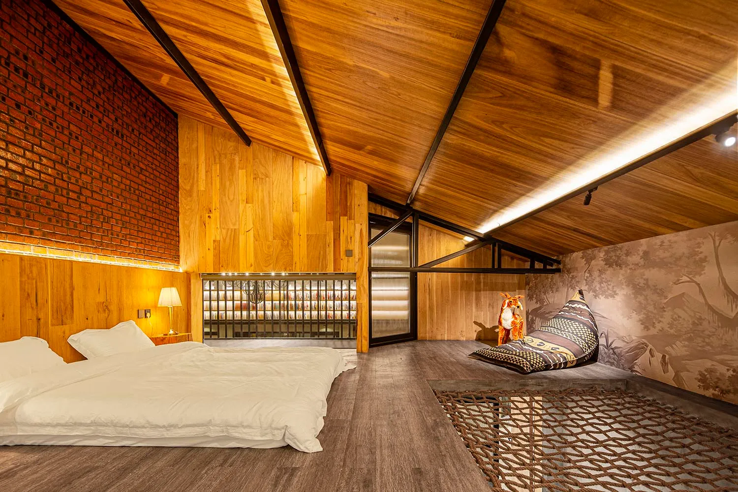 Modern bedroom with wooden walls, floor, and ceiling, featuring a bed and a cozy sitting area with a pillow and a fox figurin