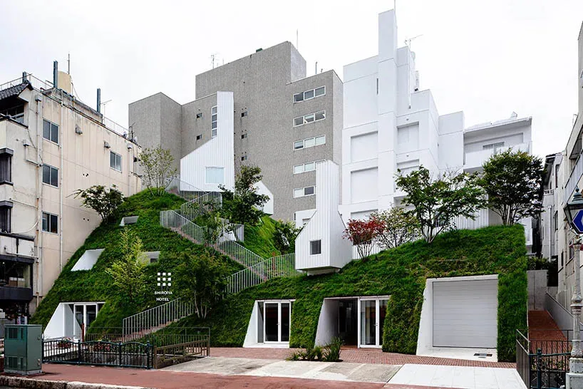 A modern residential building featuring a green roof, surrounded by greenery and buildings.
