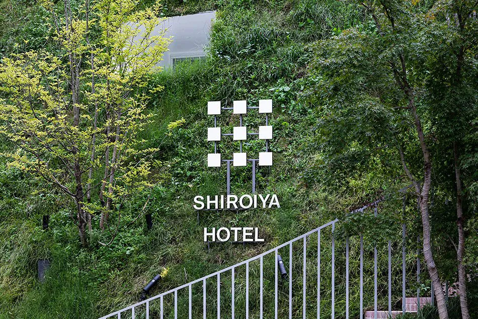 A metal sign with the words 'SHIROIYA HOTEL' embedded in green foliage.