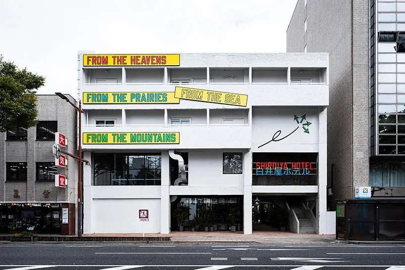 A modern architectural building exterior painted white, featuring text banners with the phrase 'From The Heavens', 'From The 