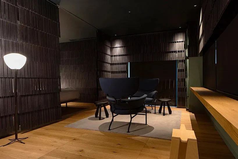 A modern living room with wooden flooring, a black armchair with a metal frame, and dark wooden walls.