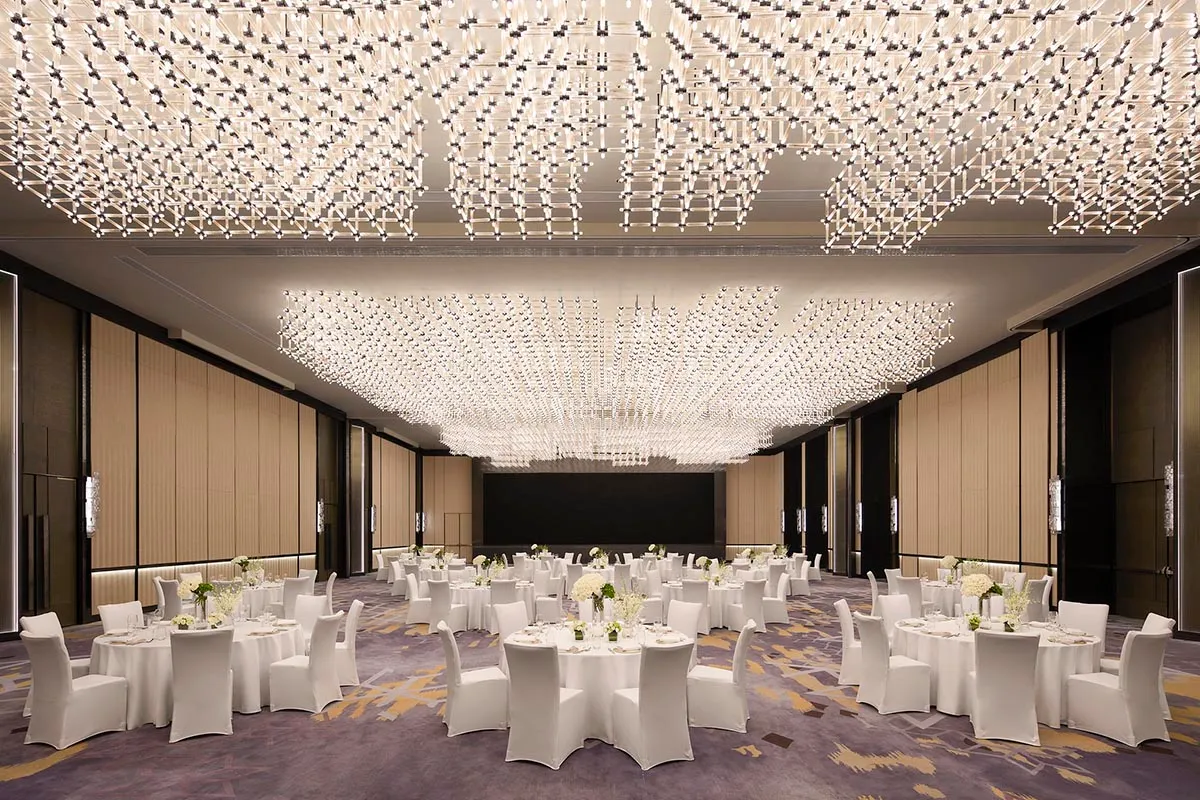 A modern banquet hall with white lighting and white tables and chairs.