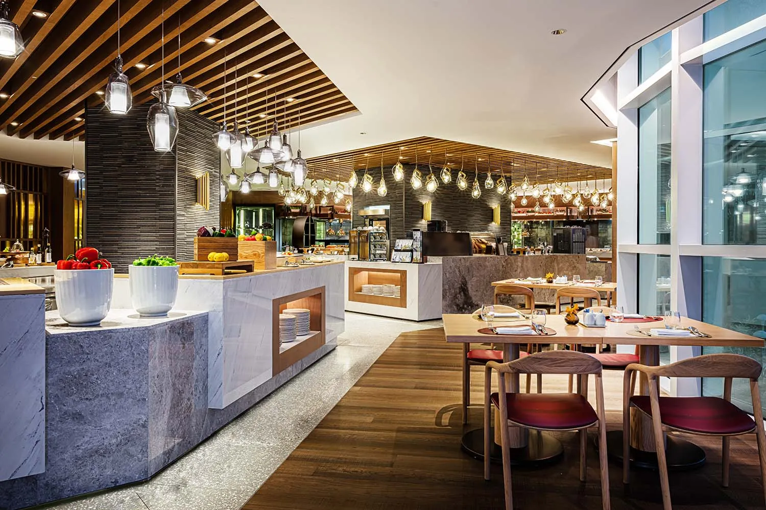 A modern restaurant interior with marble tables, wooden chairs, and glass lighting fixtures.