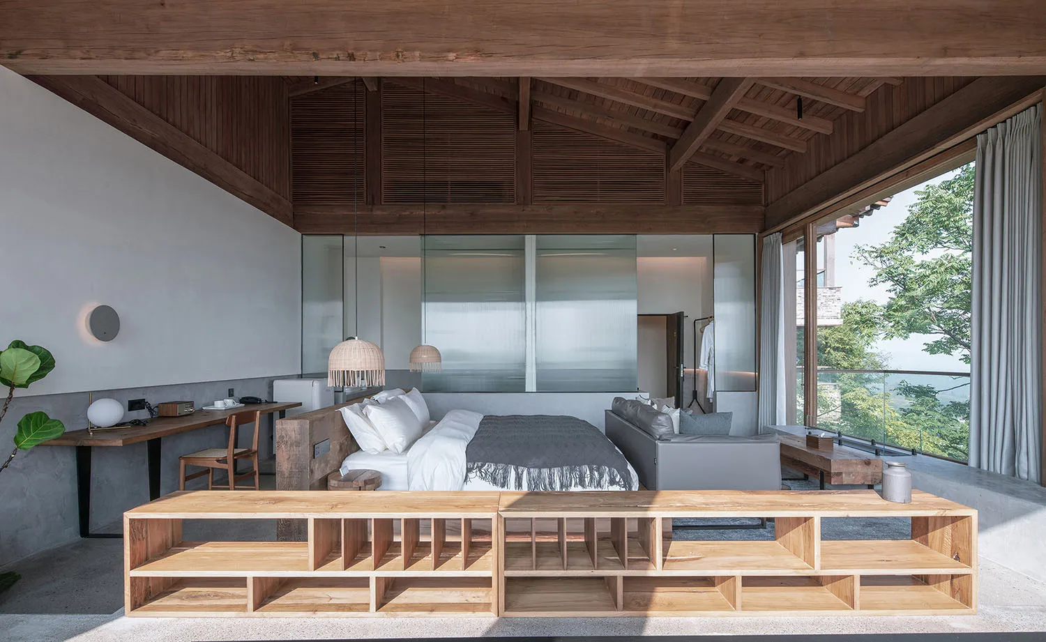 A minimalist bedroom with wooden furniture and concrete walls, featuring a large bed and a desk.
