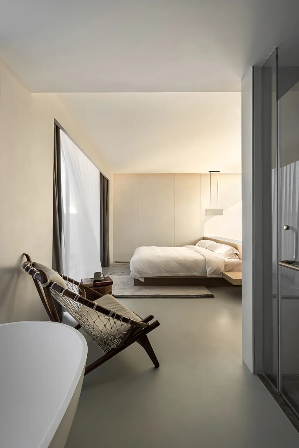 A minimalist bedroom featuring neutral-toned decor, white bedding, and a mid-century modern chair.