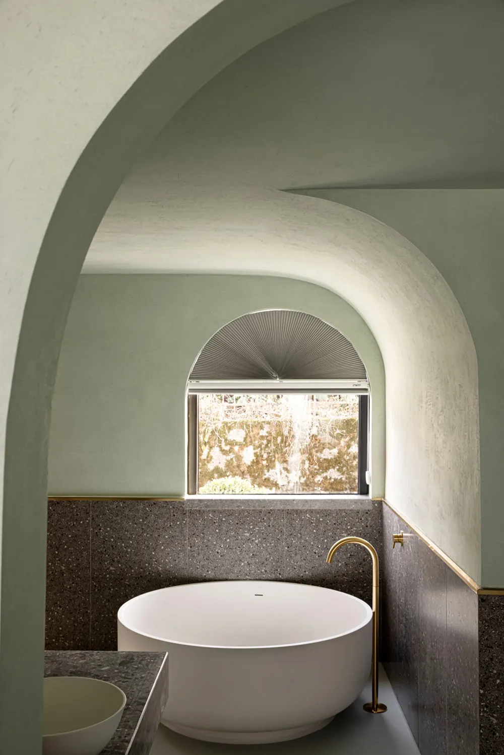 A modern bathroom with a concrete wall and a round bathtub under an arched window.