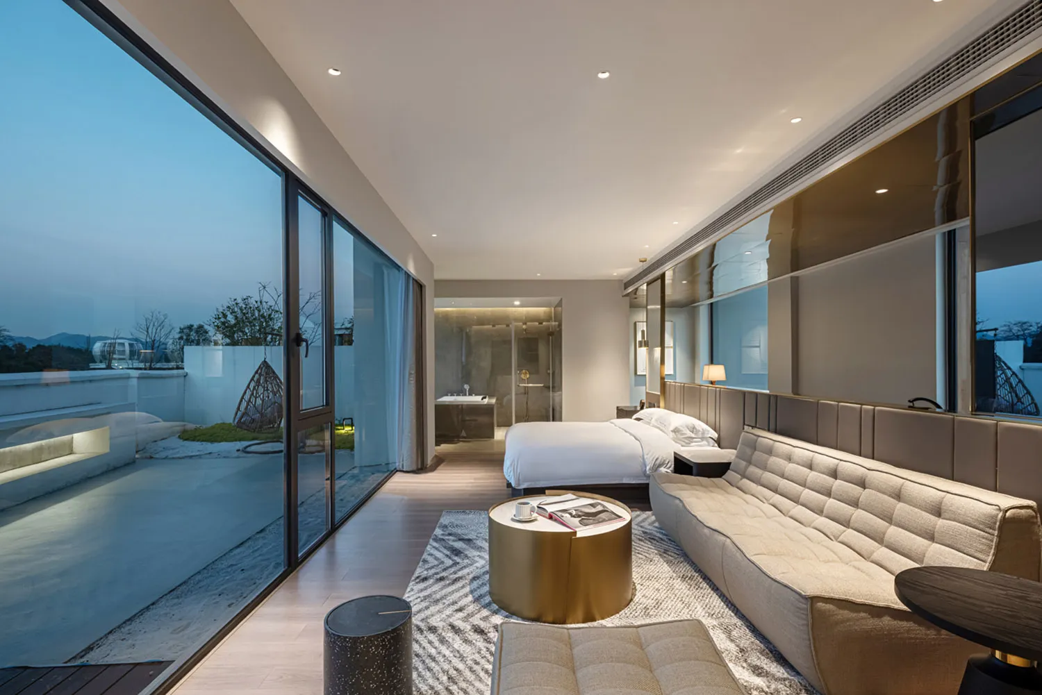 A spacious modern bedroom featuring glass walls, a large bed, and a contemporary sofa.