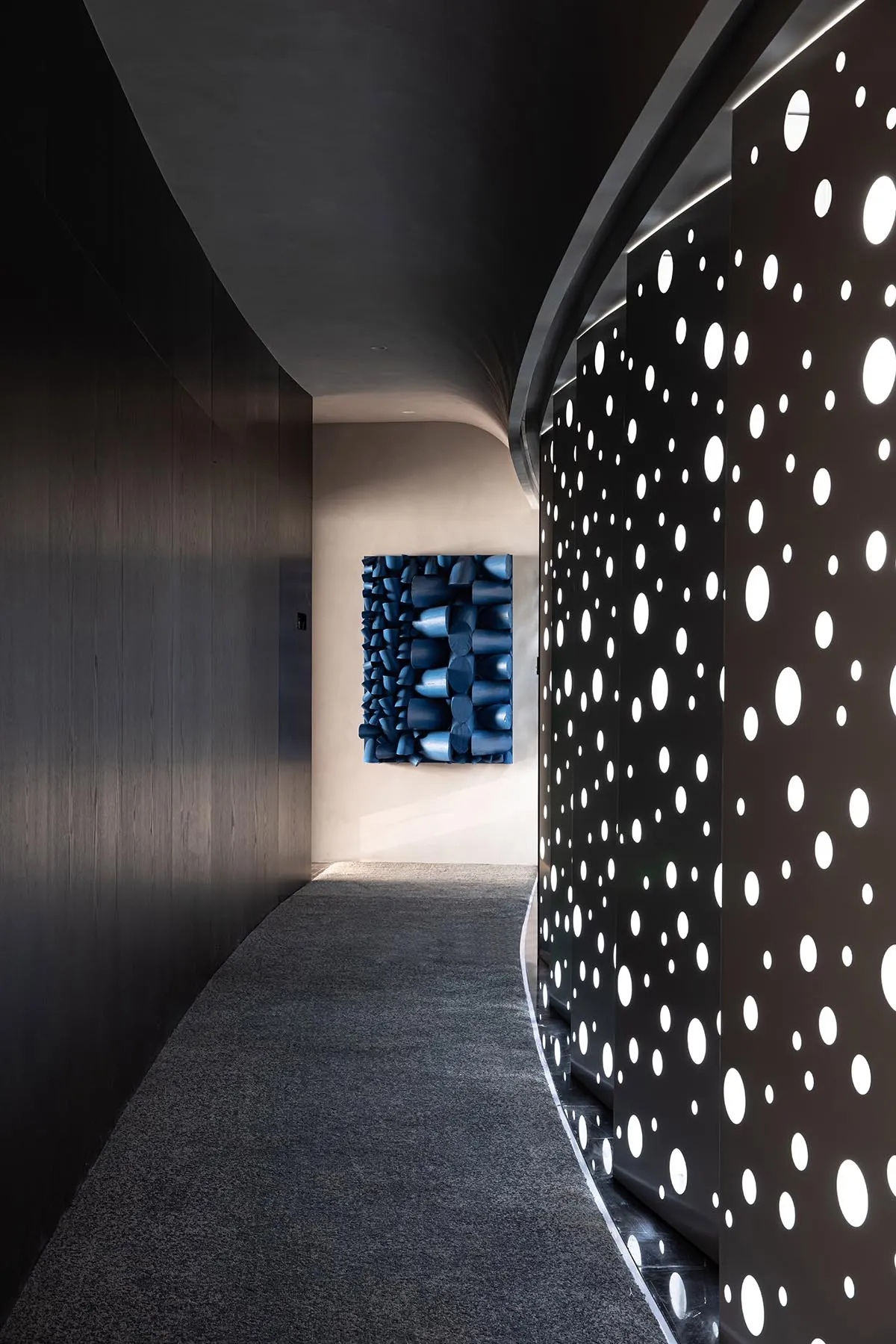 A modern, minimalistic corridor featuring a metal wall adorned with a pattern of interconnected circles.