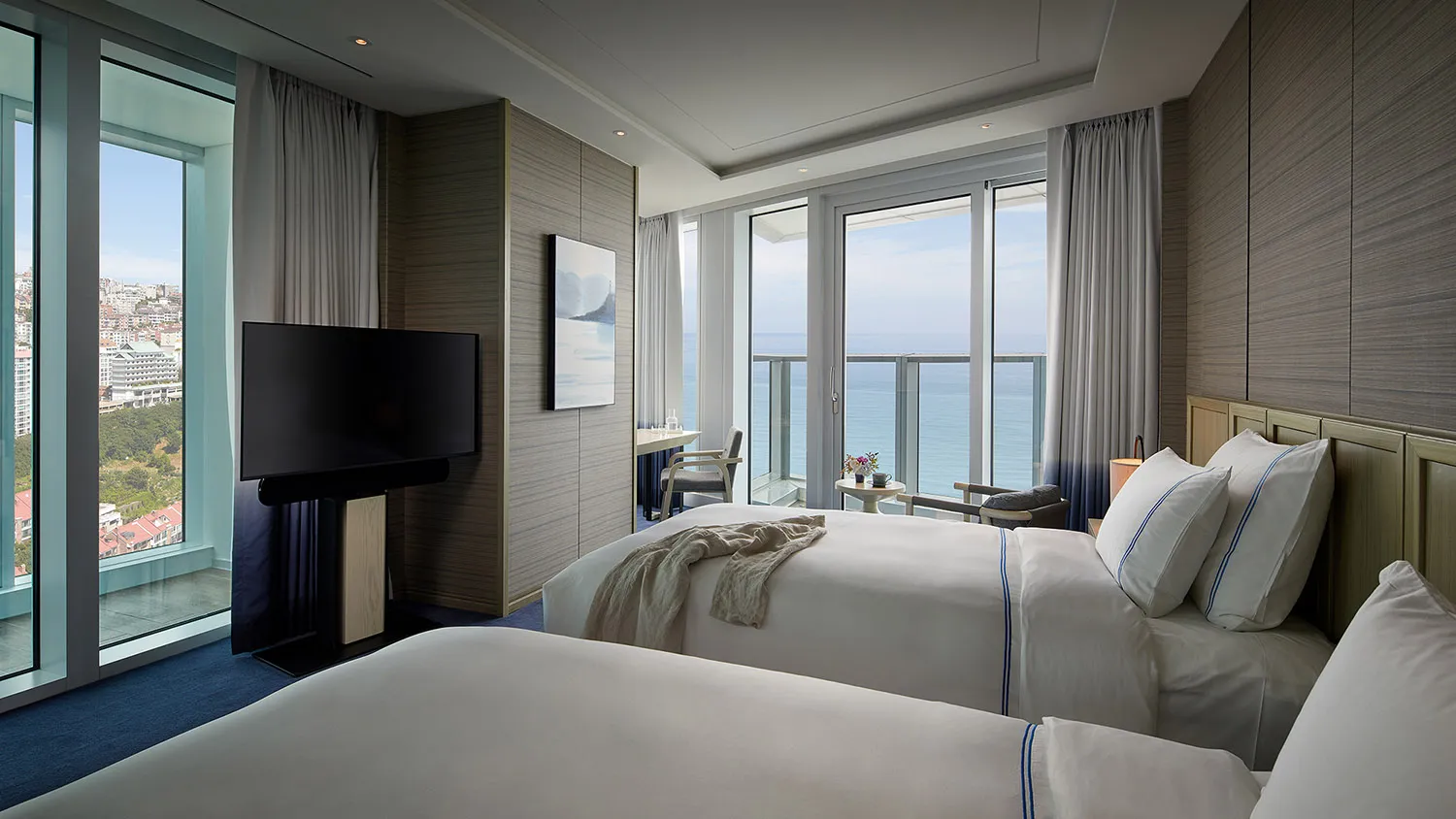Modern hotel room with twin beds, television, and ocean view.