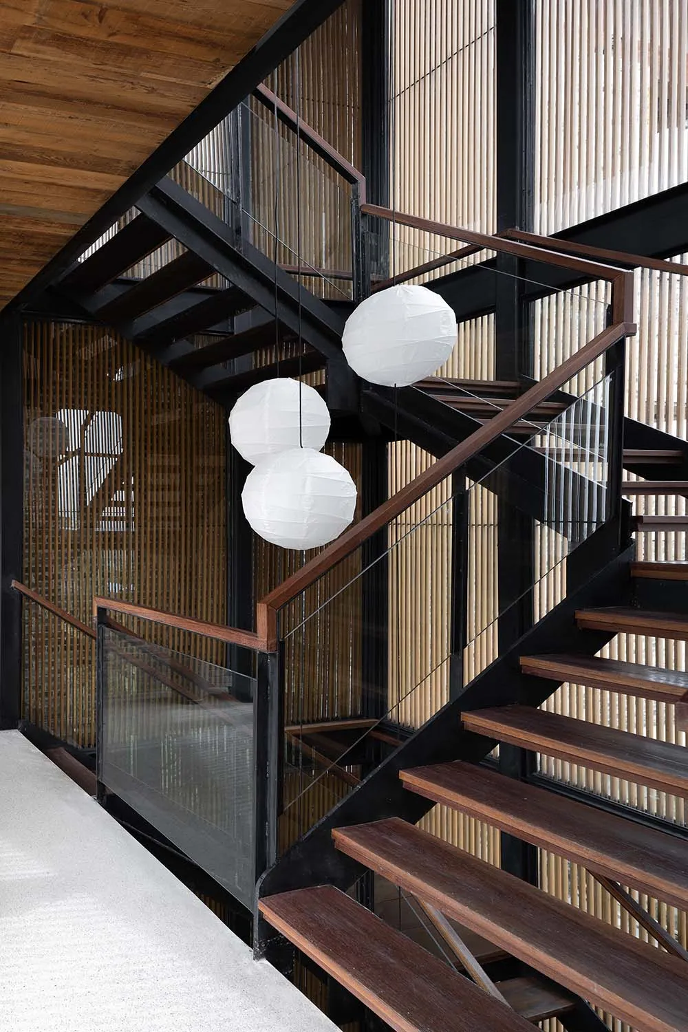A modern staircase with wooden steps, black railings, and white spherical lanterns hanging from the ceiling.