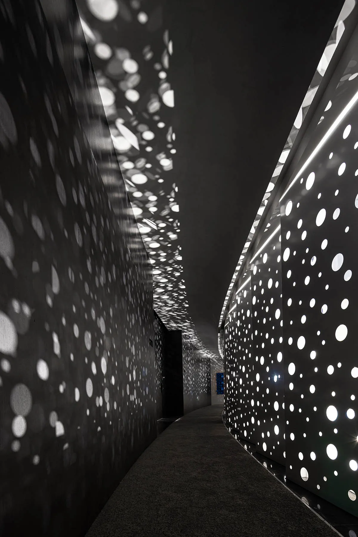 A corridor with modern lighting featuring metal perforated panels.