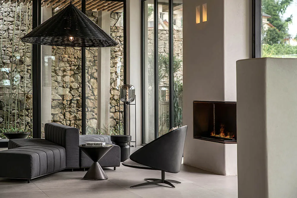 A modern living room with a concrete and stone interior, featuring a fireplace, lounge chair, and minimalist furniture.