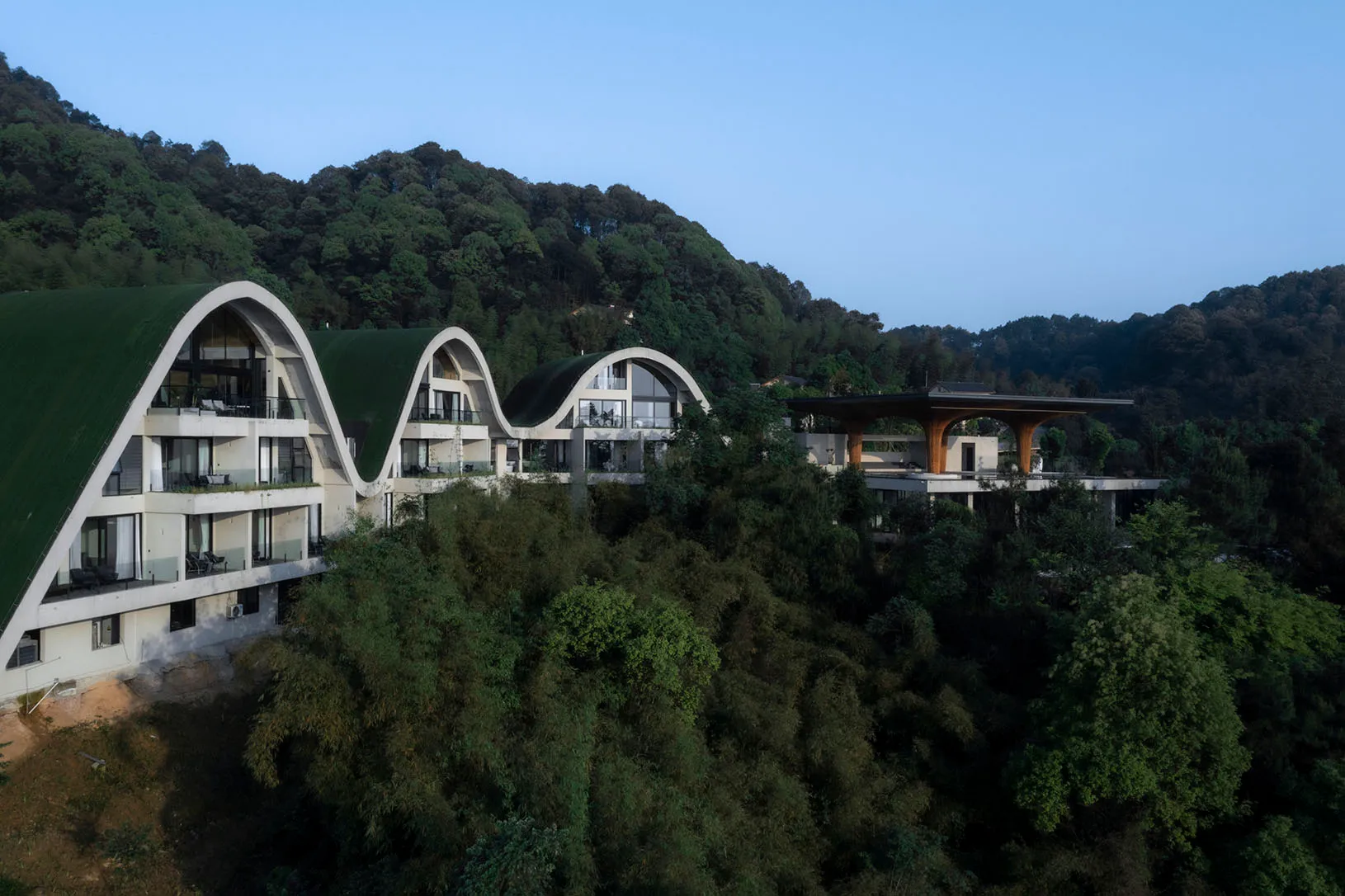 一座現代住宅度假村,擁有曲線混凝土結構,坐落於茂密綠意盎然的森林區域。