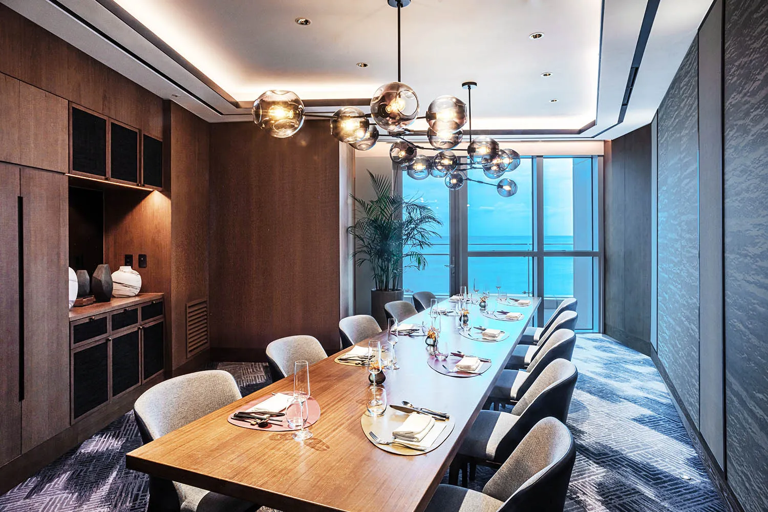 現代餐廳用餐區,擺放木製餐桌椅、吊燈,並享有海景。