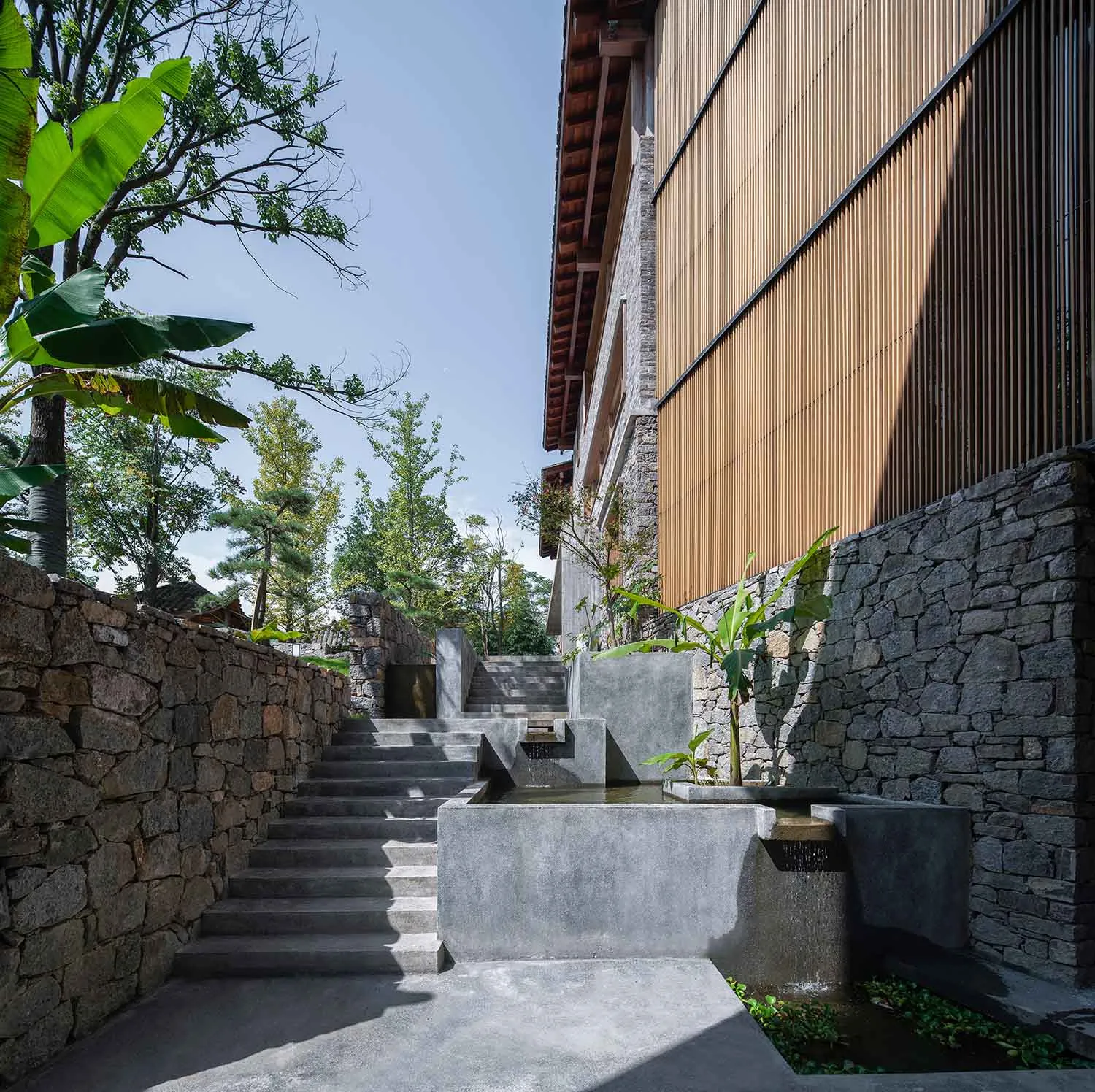 Stairs, stone fences, trees, and a building with stone walls and a concrete path.