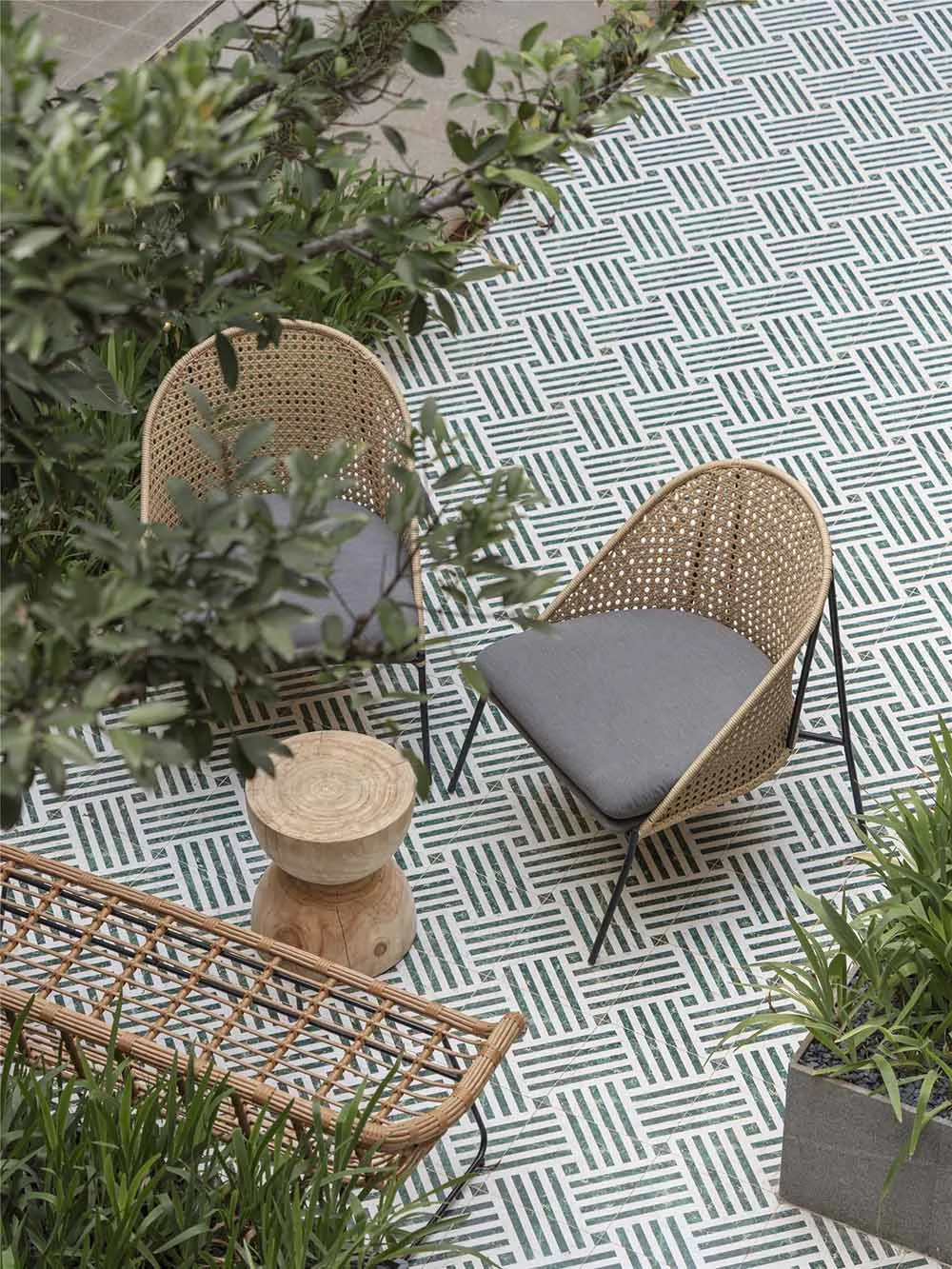 Two wicker chairs with gray cushions placed on a patterned marble tile floor outdoors.