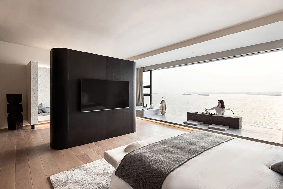 Modern minimalist bedroom with a bed, television, and large window overlooking the water.