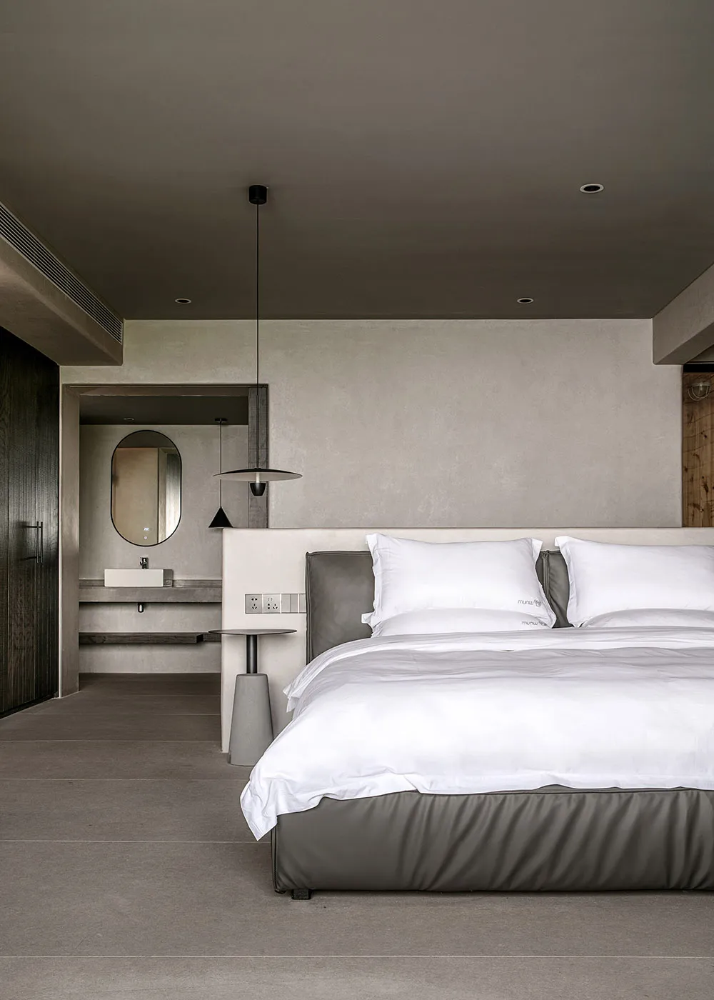 A minimalist bedroom with concrete walls, flooring, and a bed with white bedding.