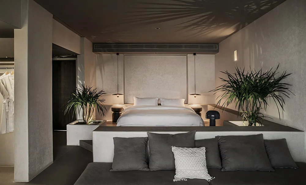 An image of a minimalist bedroom featuring a concrete bed platform and floating nightstands with leafy green indoor plants, a