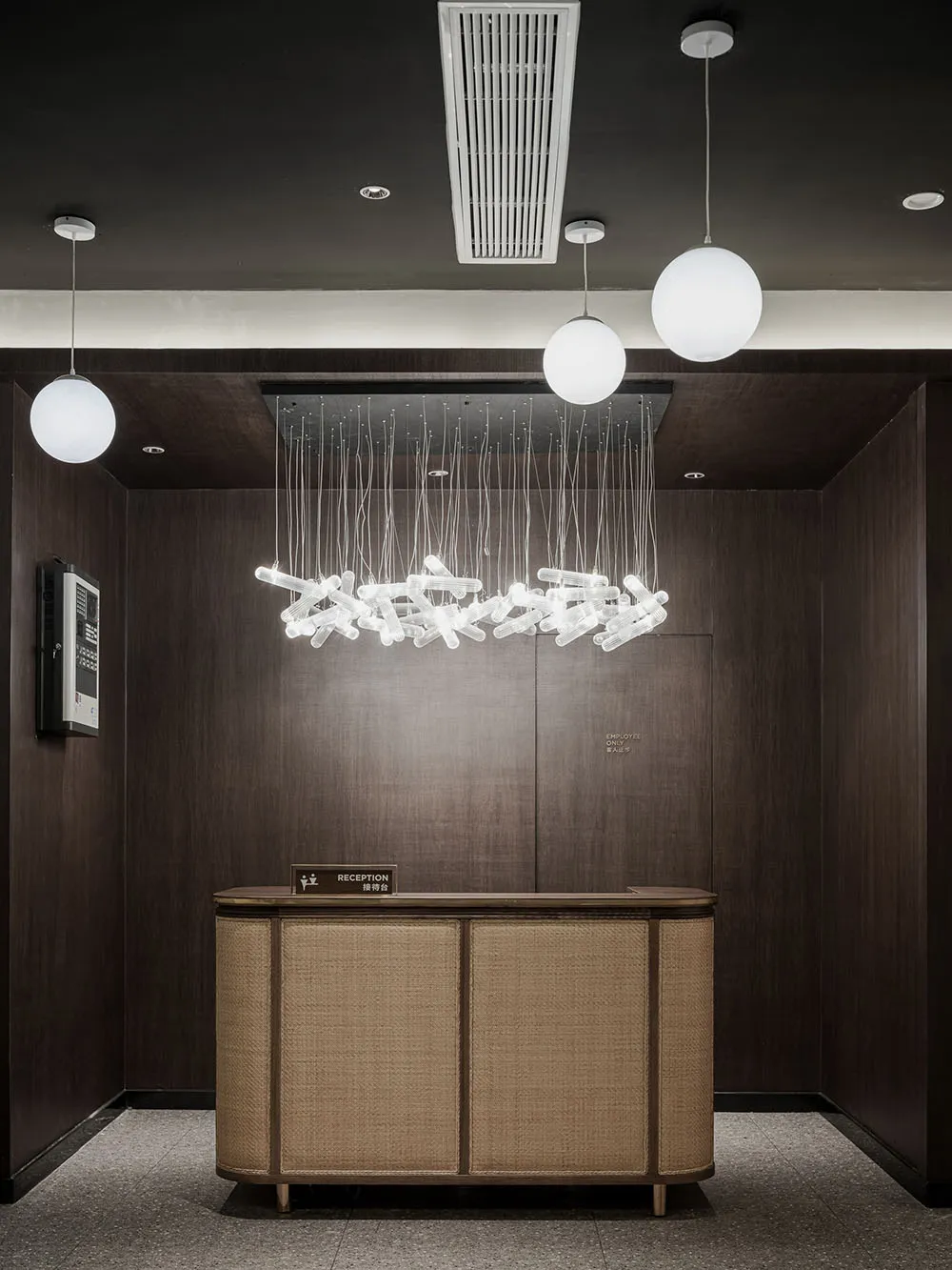 A modern reception desk with wooden, cane-inlaid panels, steel accents, and decorative lighting fixtures.