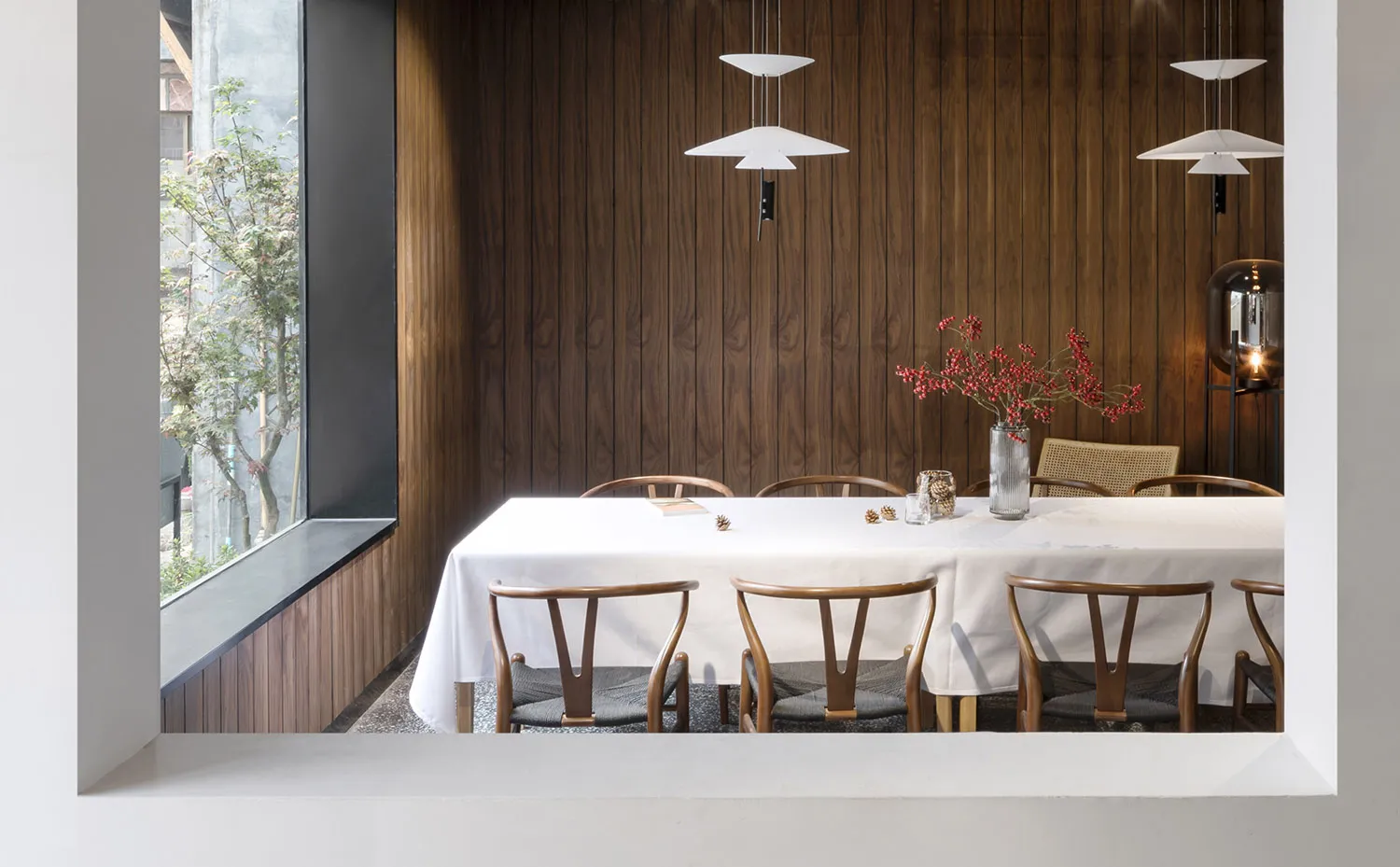 A modern restaurant interior with wooden panels on the walls, a white tablecloth covering the dining table, and a centerpiece
