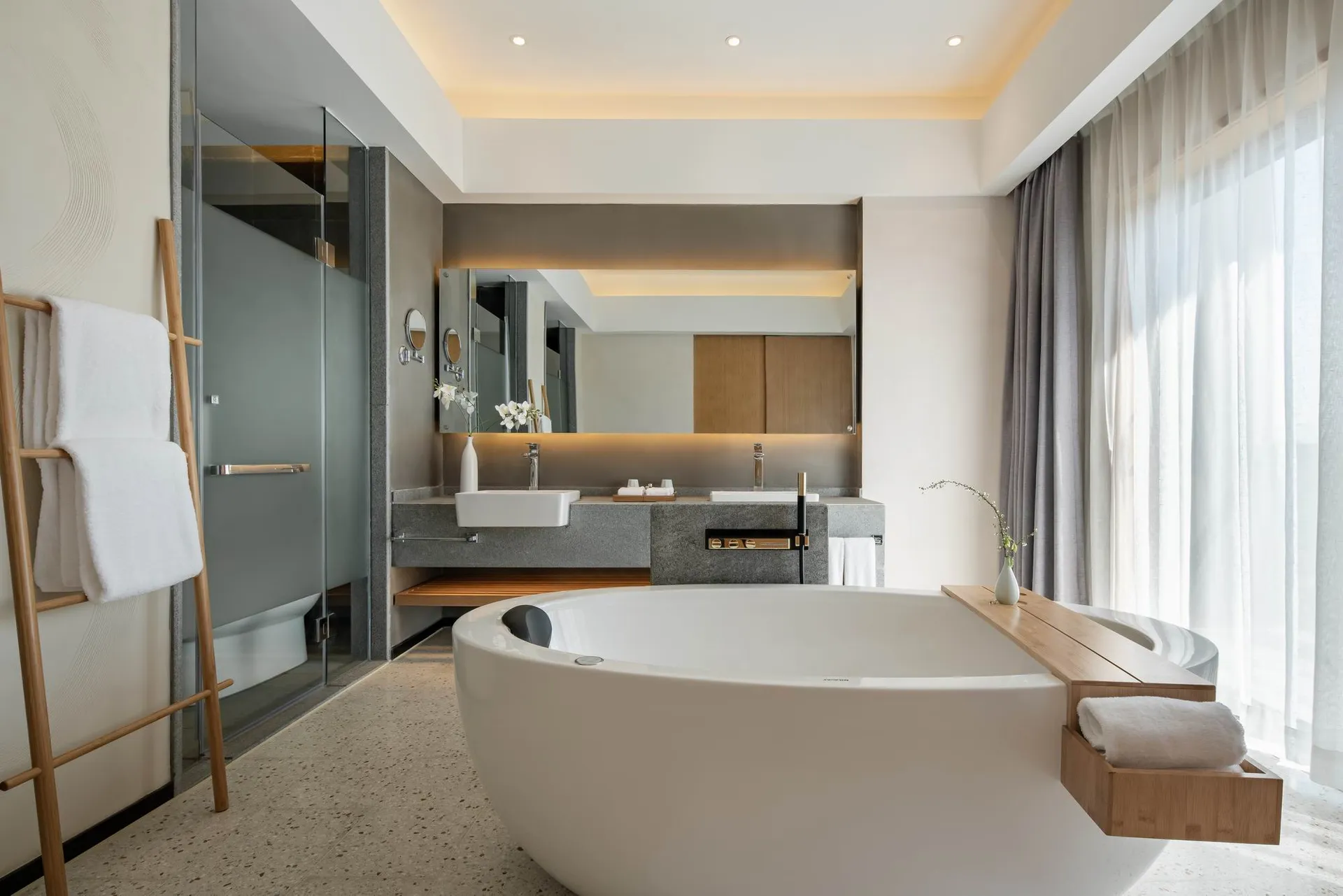 A modern minimalist white bathroom with a large freestanding tub, a double sink vanity, and a glass-enclosed shower.