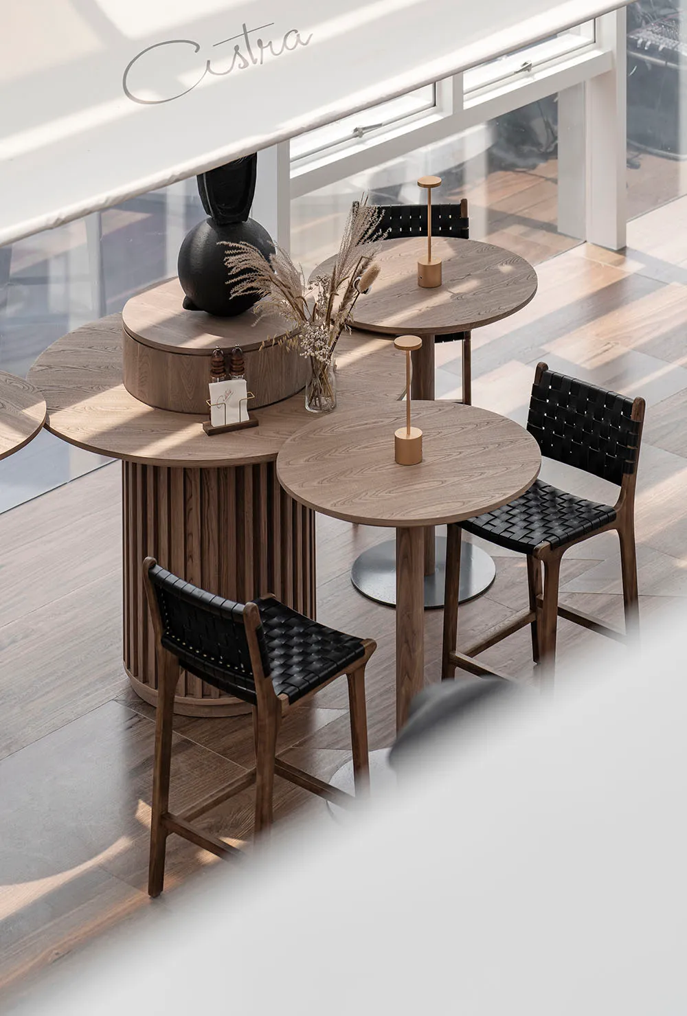 Modern cafe with round wooden tables and black woven leather chairs.