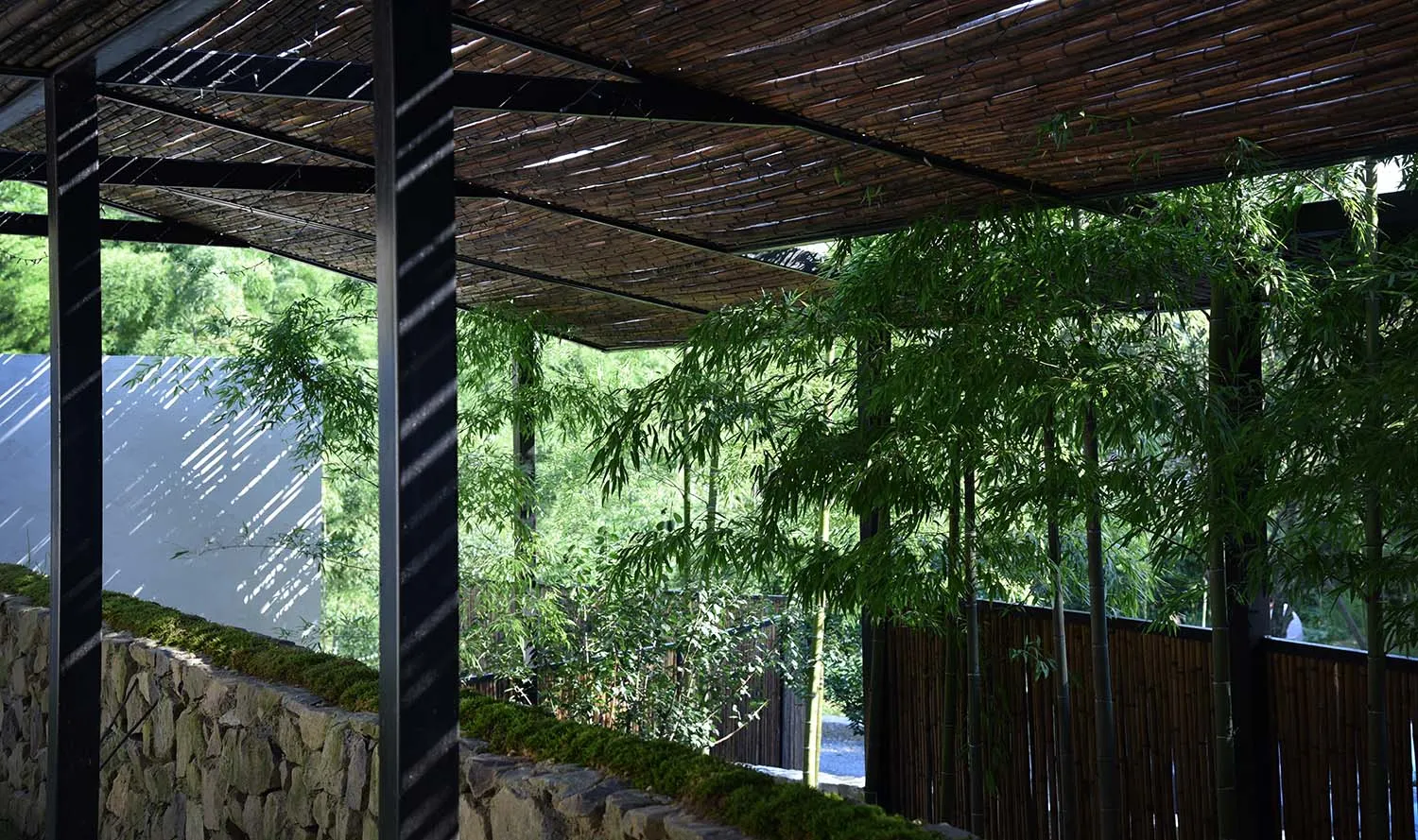A modern garden featuring a bamboo shade structure with a natural stone wall and greenery.