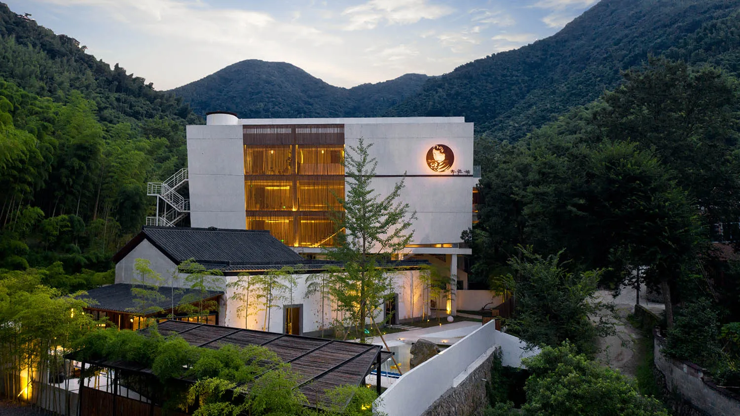 Modern, minimalist hotel resort with white stucco and glass exterior located amidst lush green mountains.