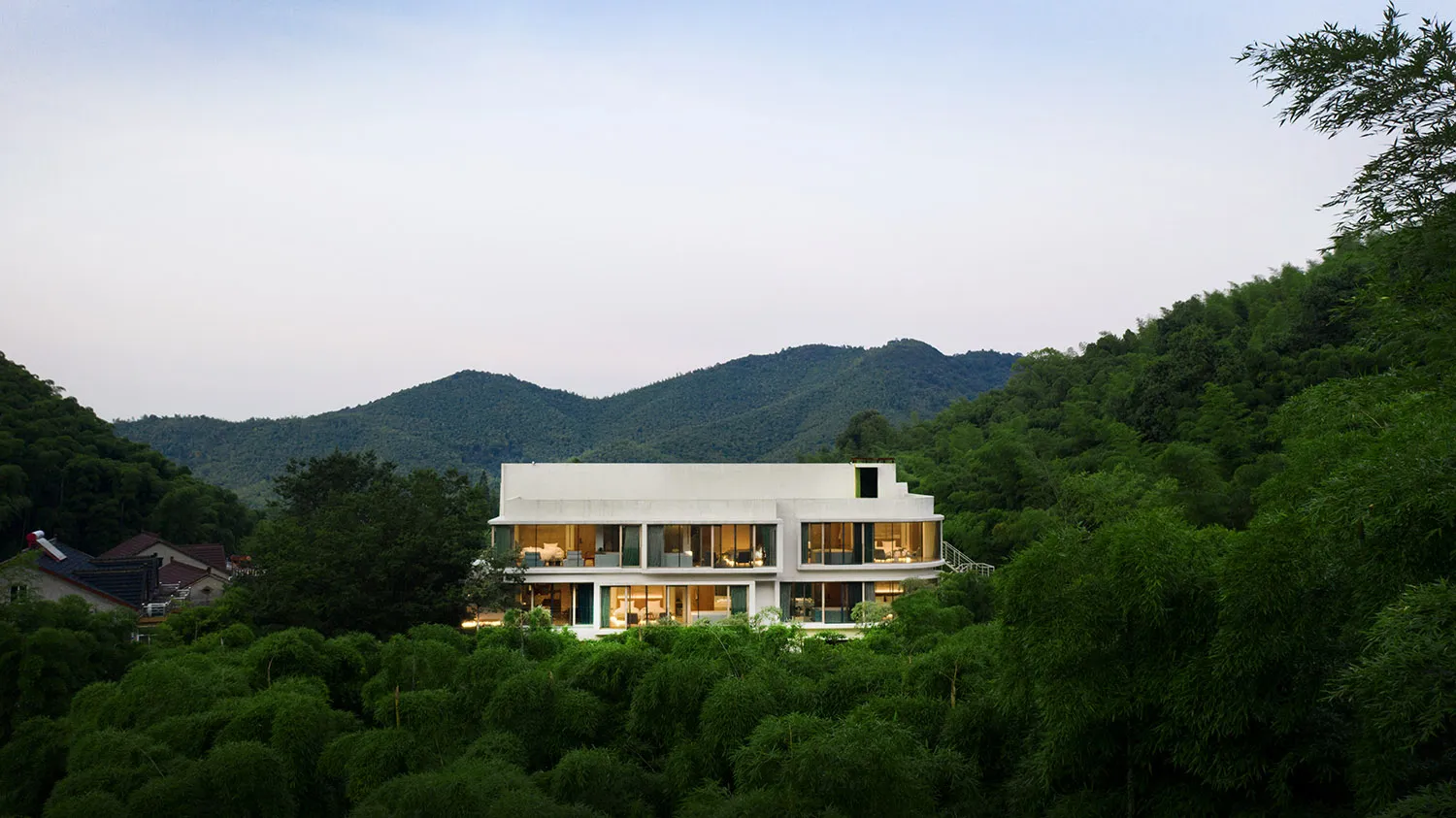現代住宅白色牆面，四周環繞綠樹，背景為山巒景色。