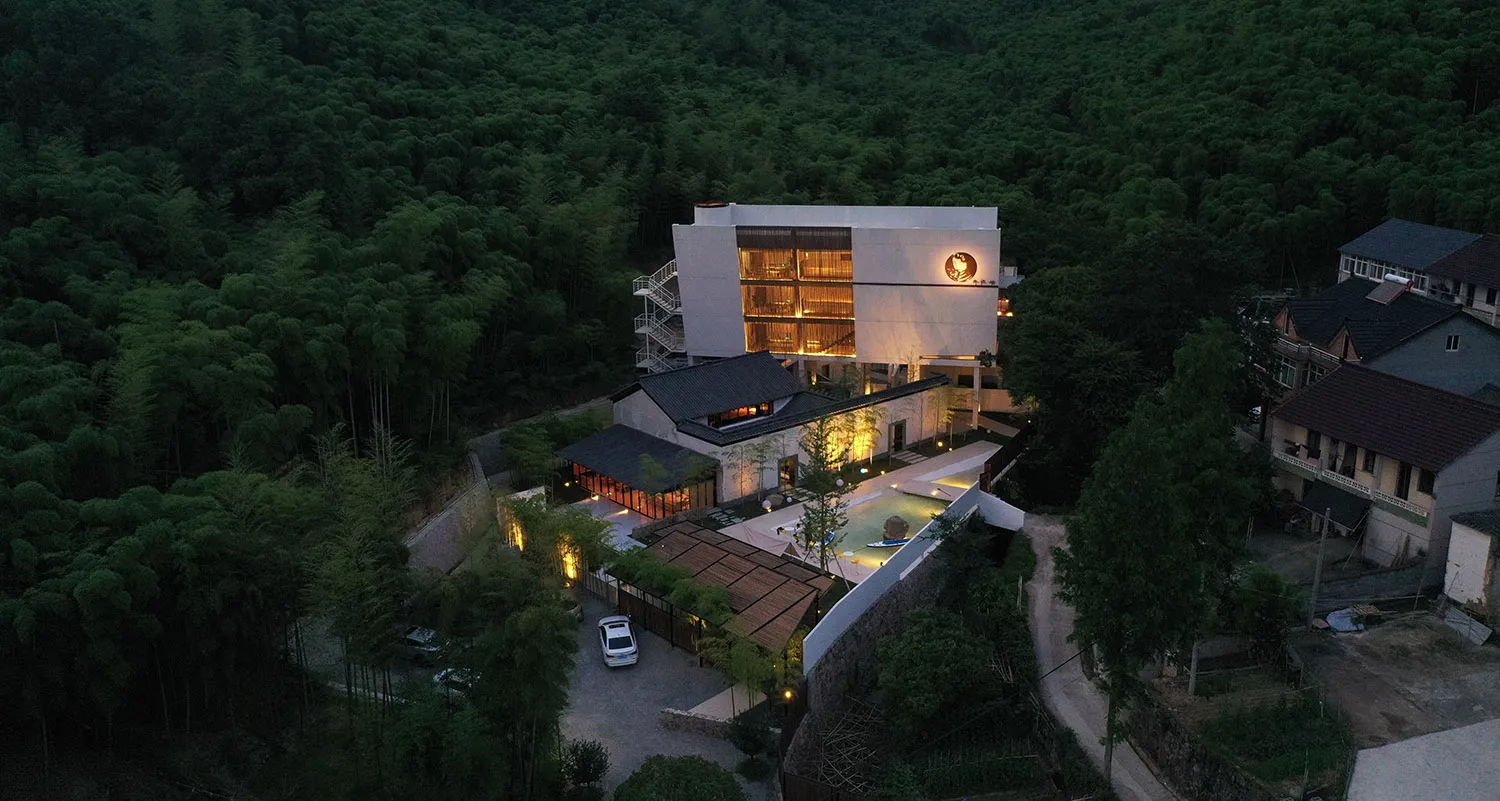 A modern residential space illuminated at night, with concrete structures, glass windows, and warm interior lighting.