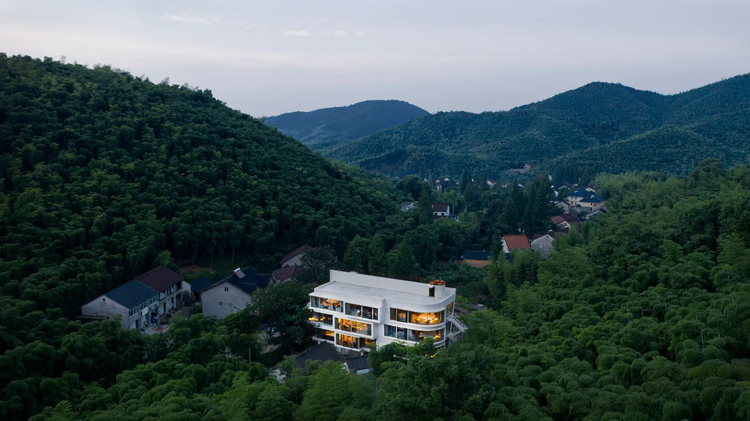 一棟現代白色住宅坐落於綠意盎然的森林山坡上。
