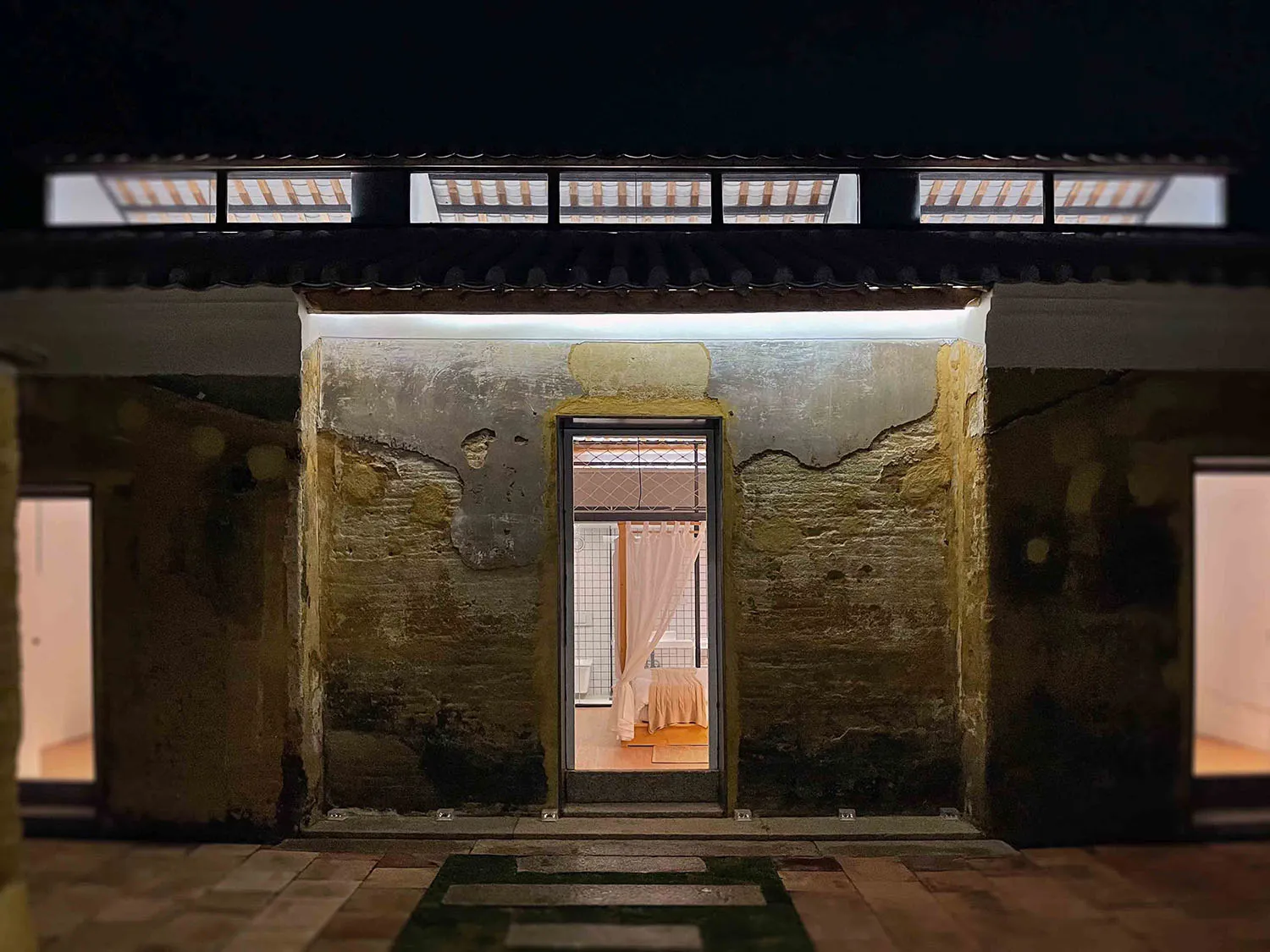 A night view of an old stone house with a lit doorway, showing interior elements.