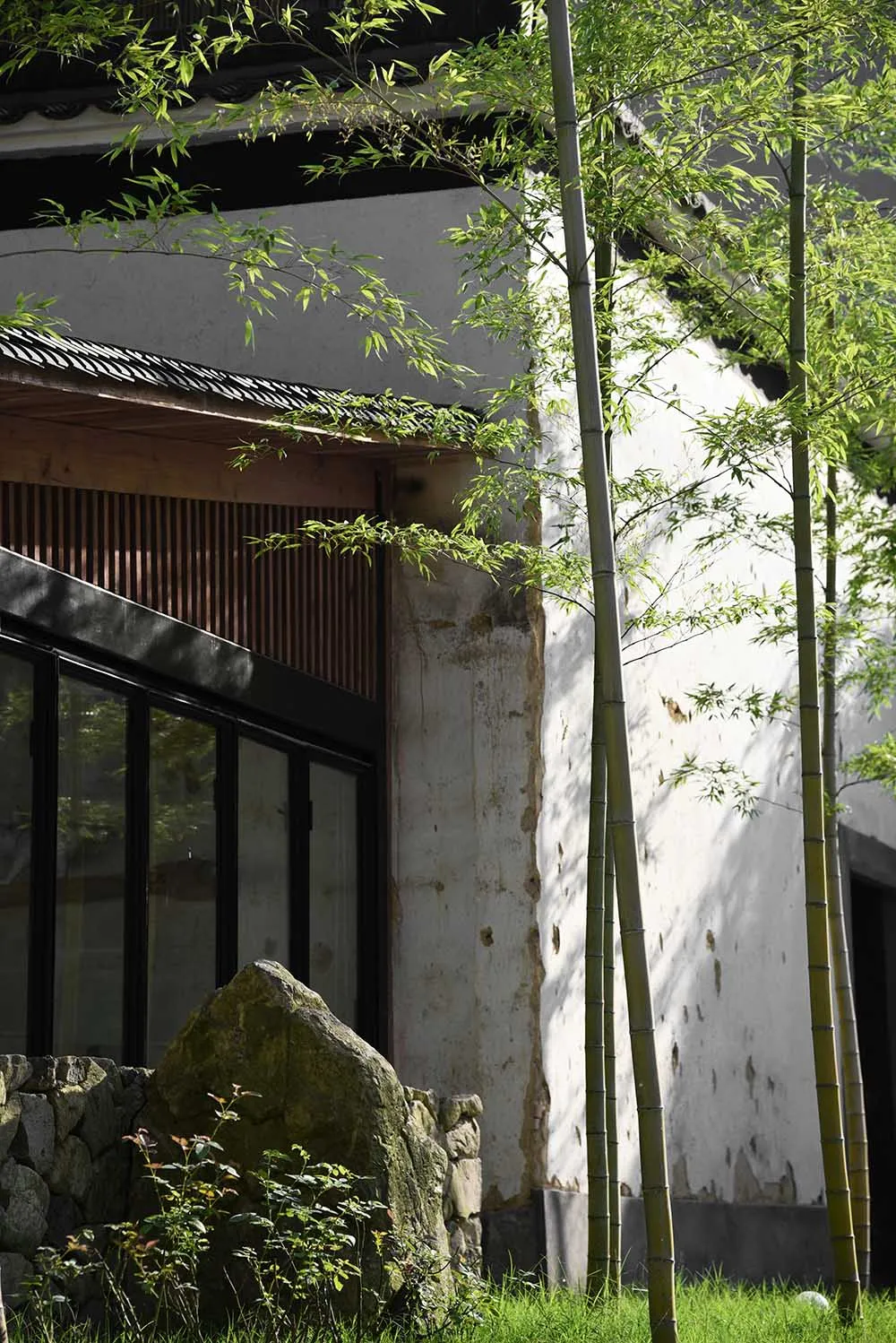 A stone and bamboo exterior of a building with tall green bamboo trees beside it.