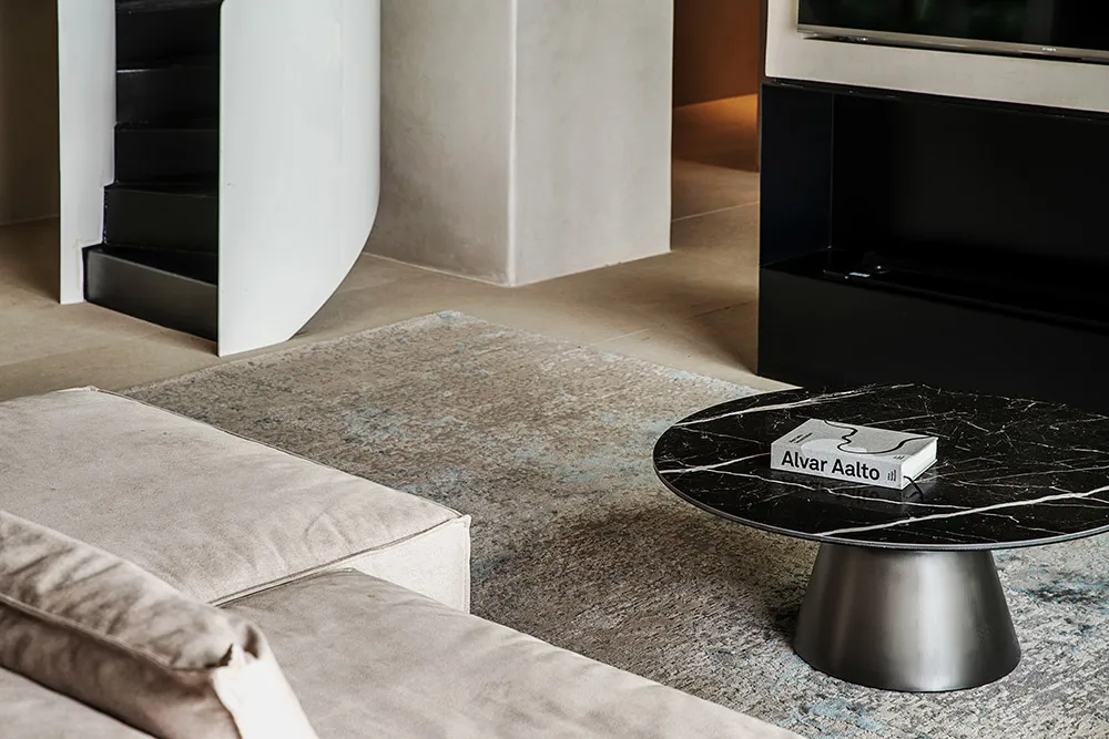 A modern living room featuring a marble coffee table with an Alvar Aalto book on it, a light-colored sectional sofa, and a sl