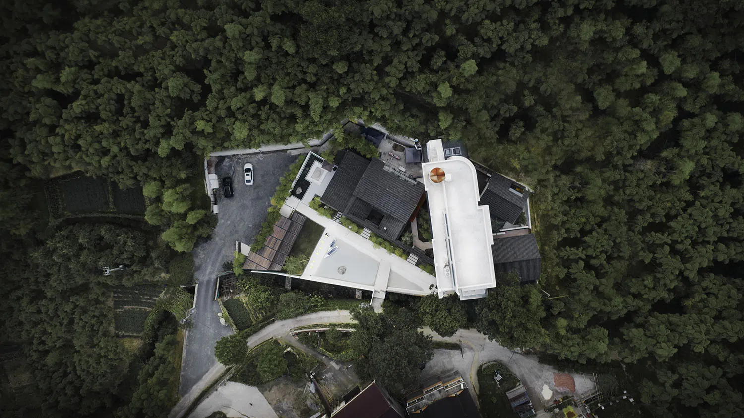 Aerial view of a modern residential house surrounded by dense greenery, featuring a white rooftop.