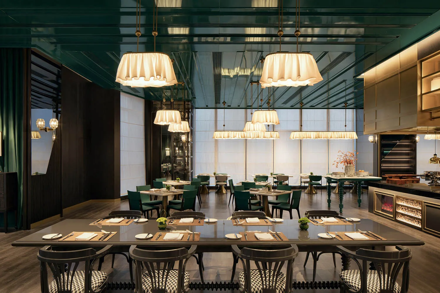 A modern restaurant dining room with large windows, green pendant lights, and meticulously set tables.
