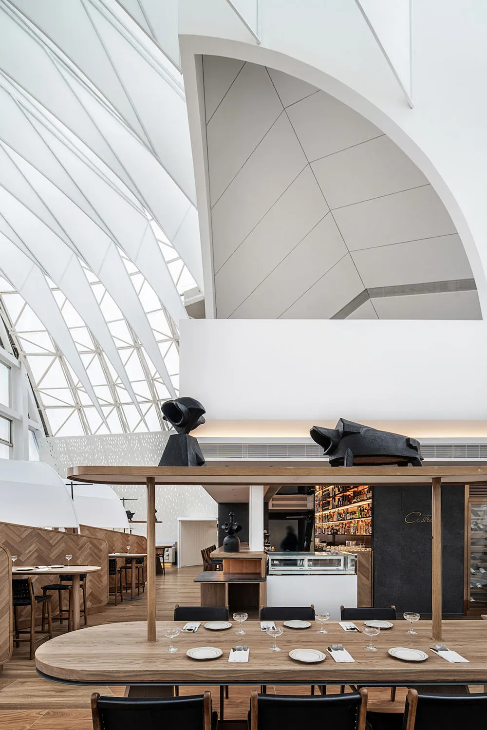 Modern restaurant interior with white walls, wood tables, concrete floor, and metal accents.