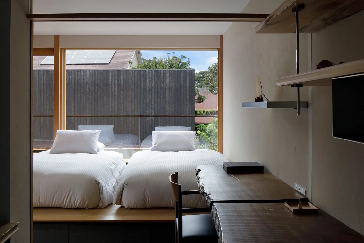 A minimalist bedroom with twin beds dressed in white linens, surrounded by wood accents and natural light.