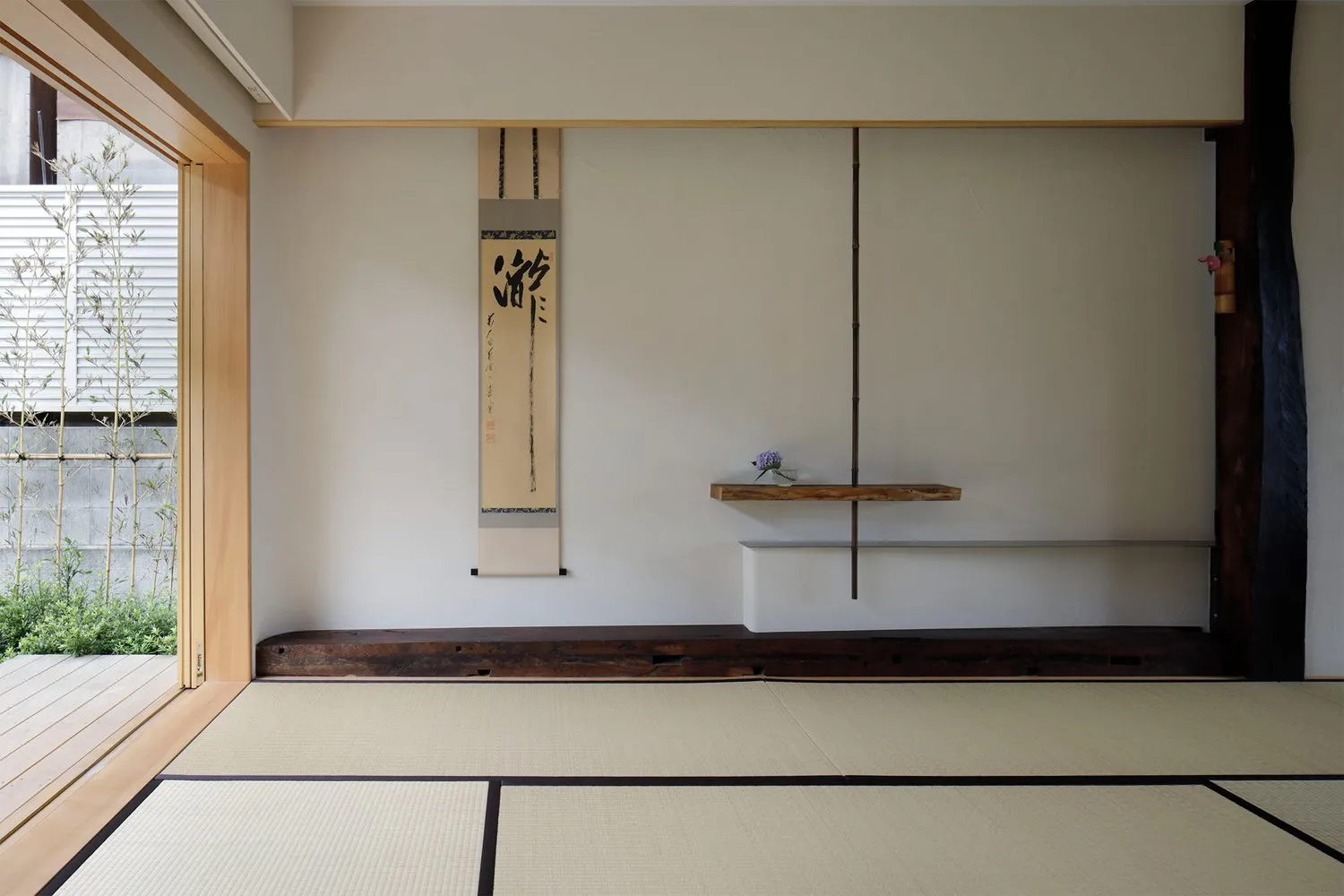A minimalist living room with a wooden floor and tatami mats, featuring a simple yet elegant design with decorative plants an