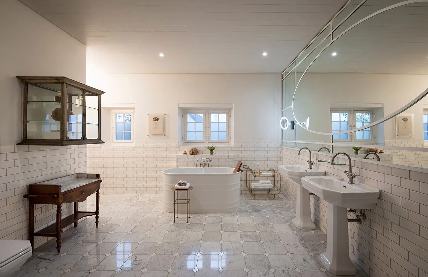 A modern bathroom with white tiles, marble floors, and a large white bathtub.