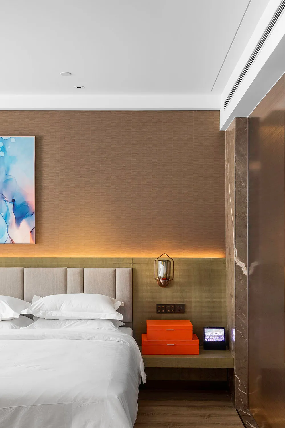 A modern bedroom featuring textured walls, a neatly made bed, a floating nightstand with orange boxes, and a wall-mounted lam