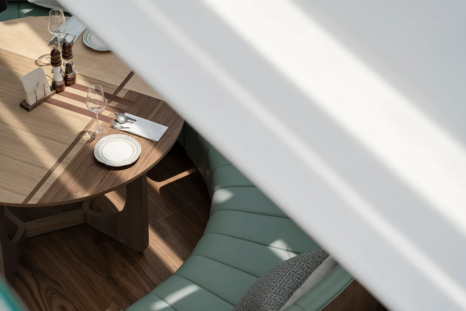 Modern dining room with wooden furniture and curved seating, featuring a round wooden table, cutlery, and white tableware.