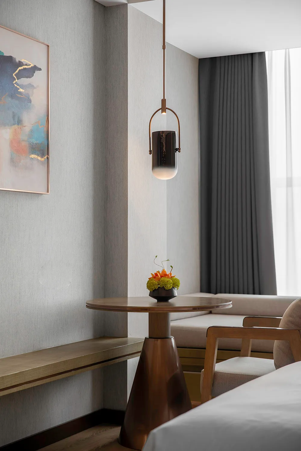 A modern minimalist bedroom featuring a wooden table with a small plant, a hanging metal lantern, and a bed with a white blan