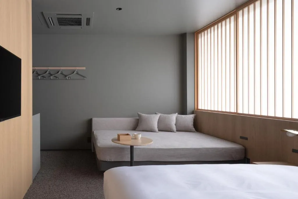 A minimalist bedroom with a white bed, a light gray couch, and a small table.